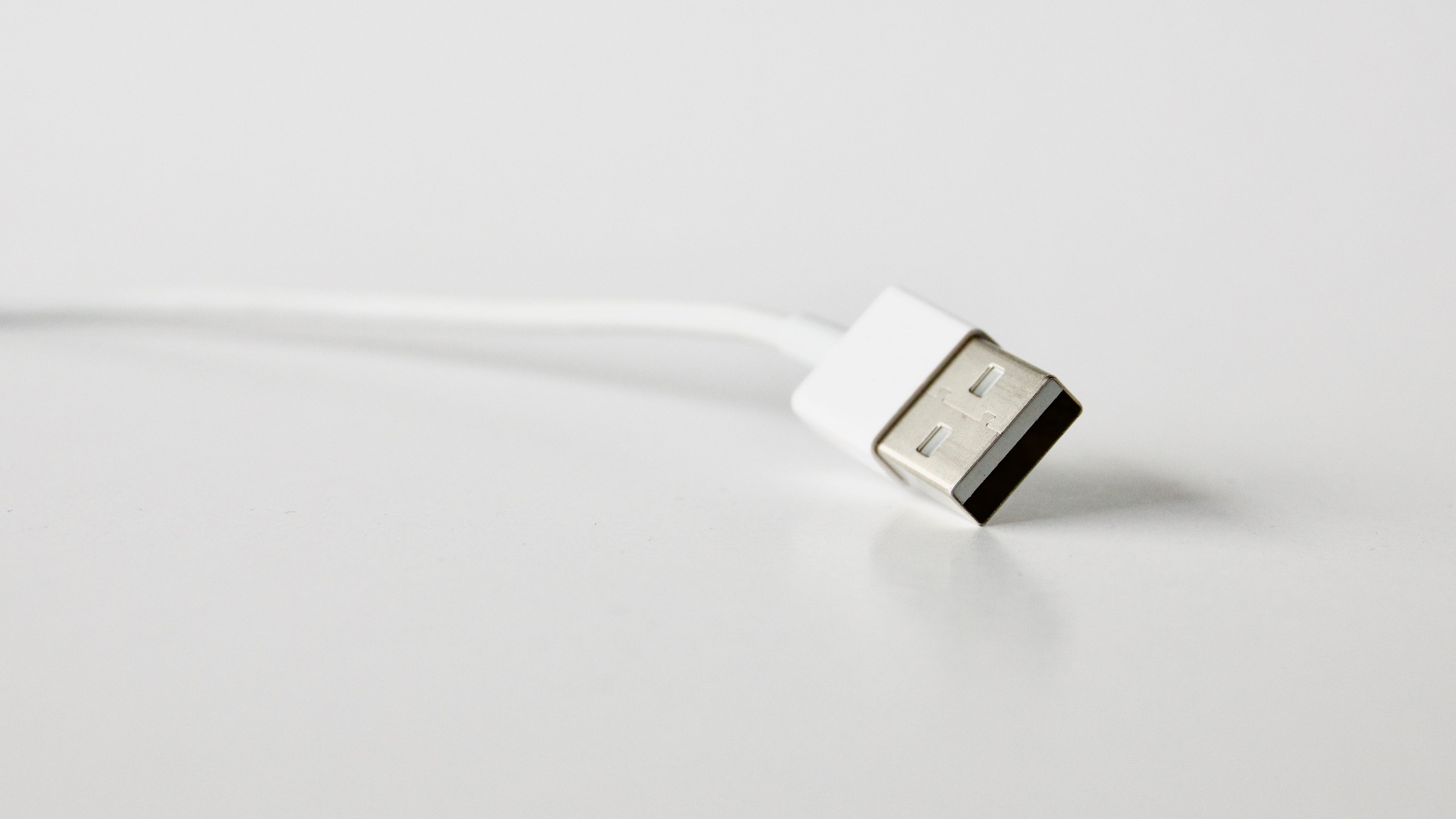 Close-up of a hand holding a small electronic device near a laptop on a table